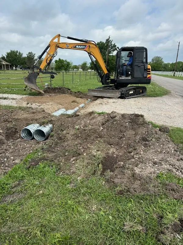 Mini excavator setting twin metal culverts at a driveway entrance