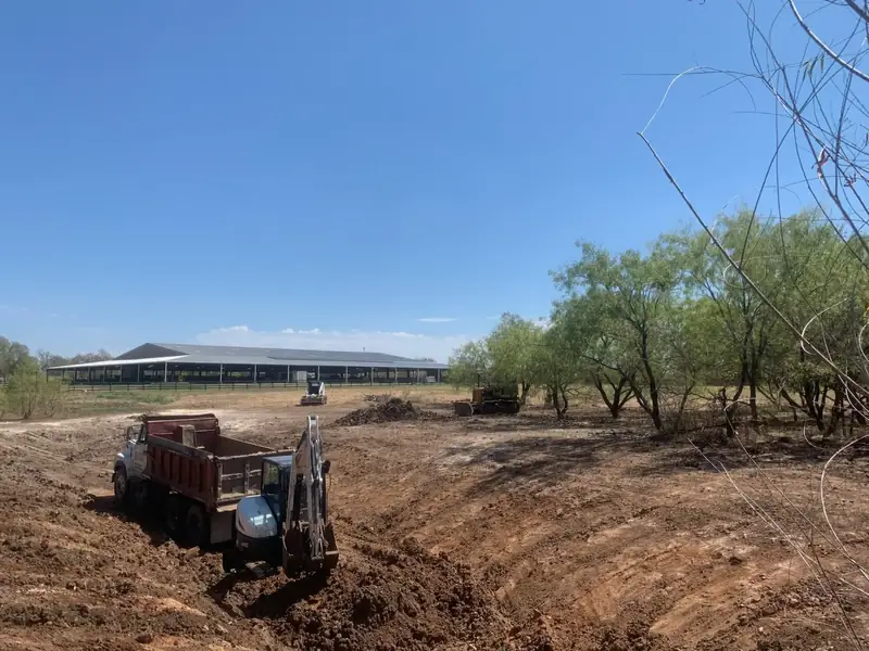 Dump truck, skid steer and dozer shaping a new pond next to a covered arena