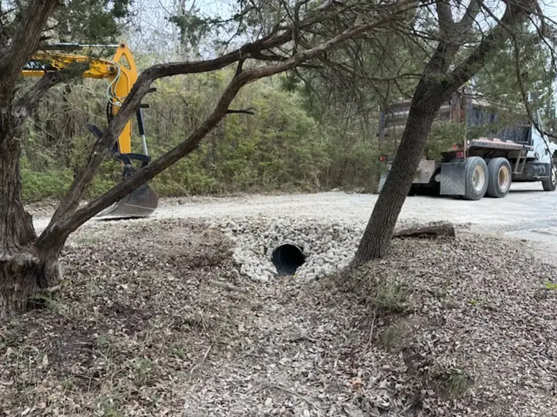 Rock-lined culvert install under the tree line with mini excavator staged behind