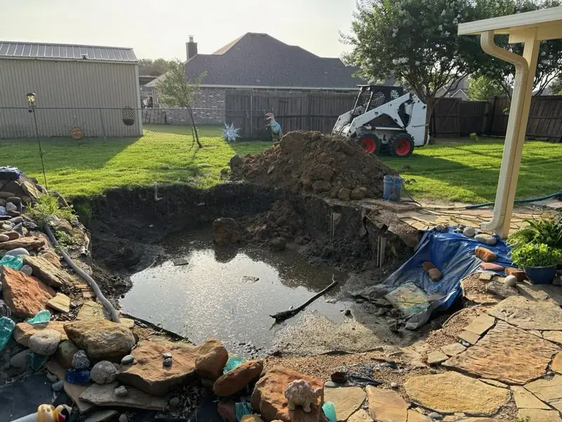 Backyard koi pond dig in progress with skid steer and stacked stone surround