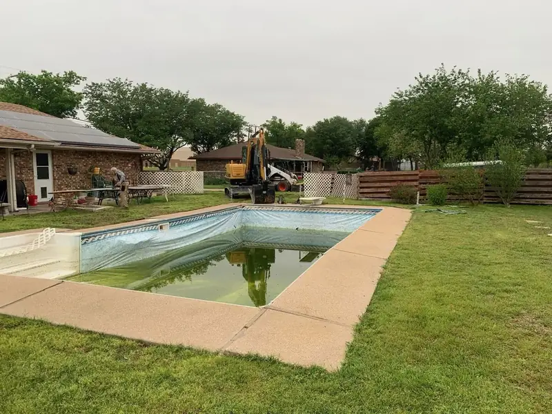 Backyard pool demolition in progress with excavator on site